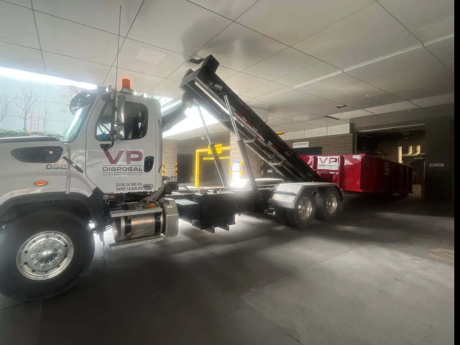 A white VP Disposal hook-lift truck in the shop with the hook arm raised