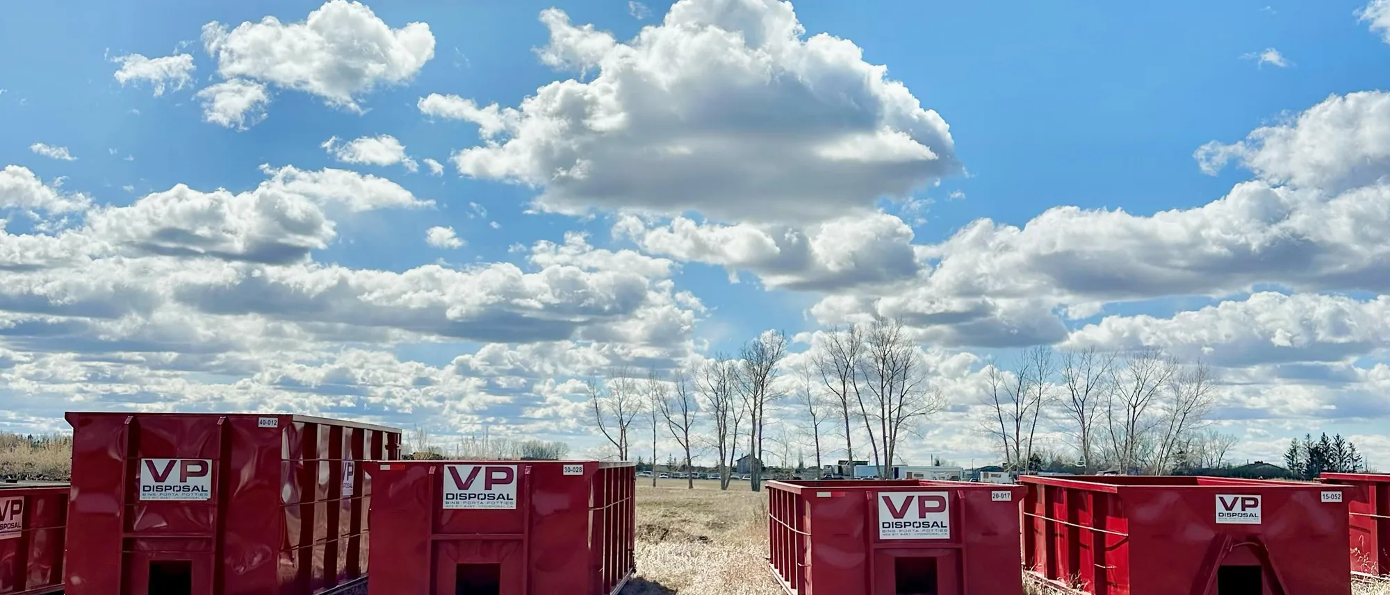 Four red VP Disposal roll-off bins of different sizes lined up in the yard under a blue sky